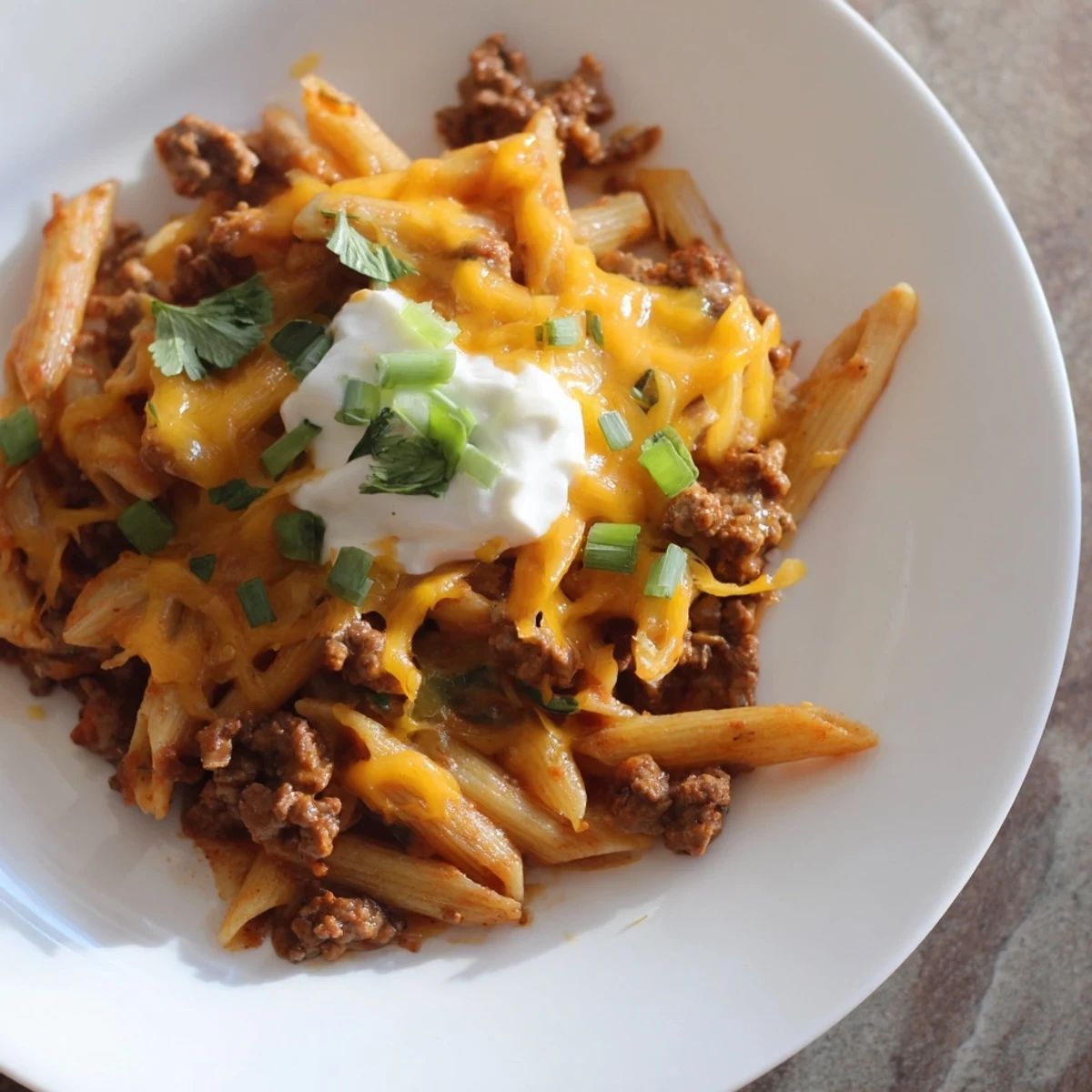A steaming bowl of Easy Beef Enchilada Pasta, garnished with cilantro and sour cream.
