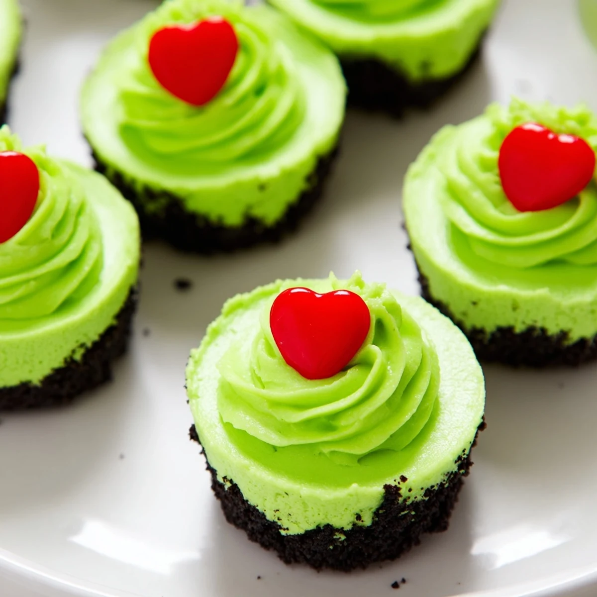 Creamy green Grinch mini cheesecakes, topped with whipped cream and festive red heart sprinkles; a delightful Christmas dessert.