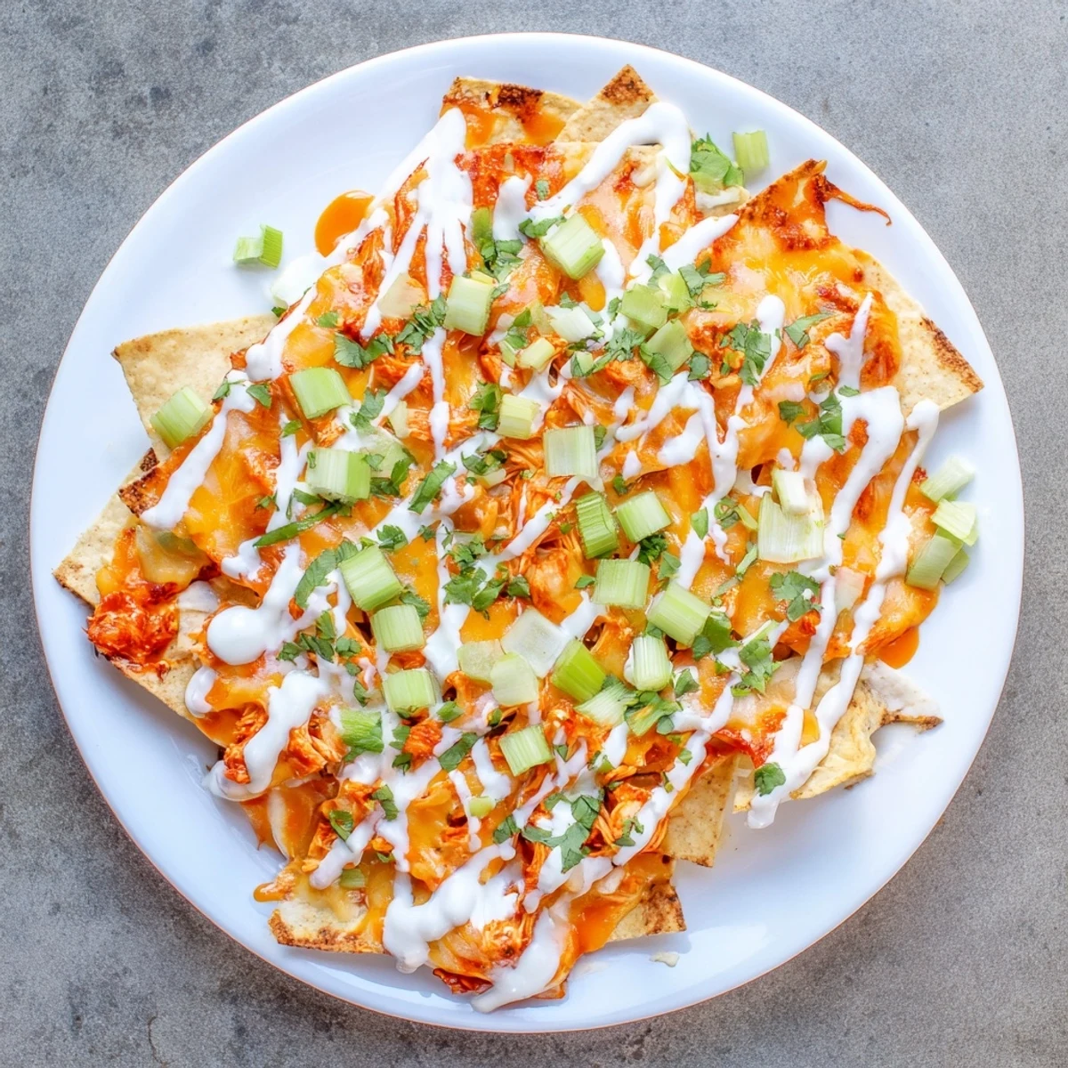 Golden-brown Buffalo Chicken Nachos loaded with shredded chicken, melted cheddar, and Monterey Jack, finished with a creamy ranch drizzle and fresh green onions.