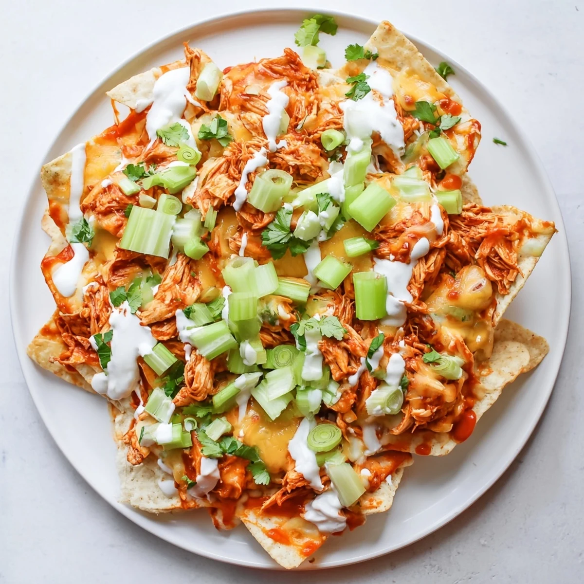 Freshly baked platter of Buffalo Chicken Nachos topped with diced celery, green onions, and cilantro, perfect for sharing during a fun game day gathering.