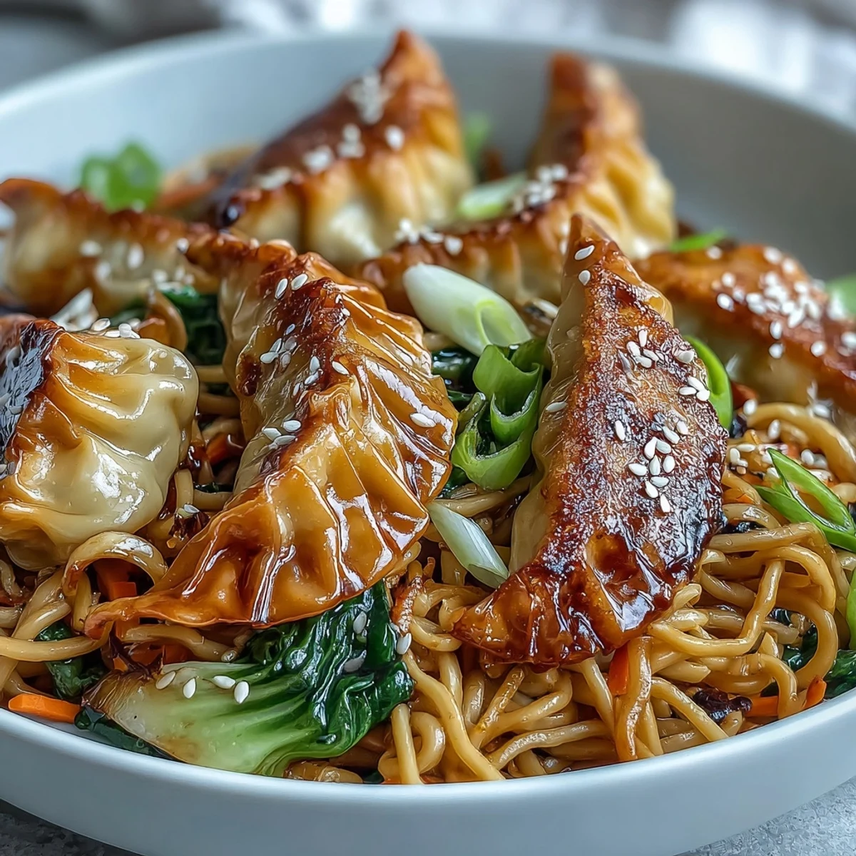 Freshly cooked potstickers rest atop a vibrant stir-fry of lo mein noodles, shredded carrots, and red cabbage in a savory garlic soy sauce.
