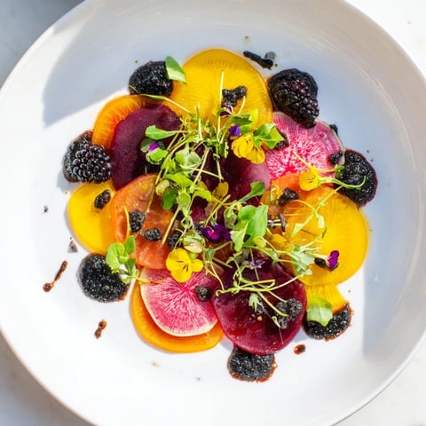 A plate of The Shadow Play appetizer features vibrantly layered beets, dark olives, and blackberries.