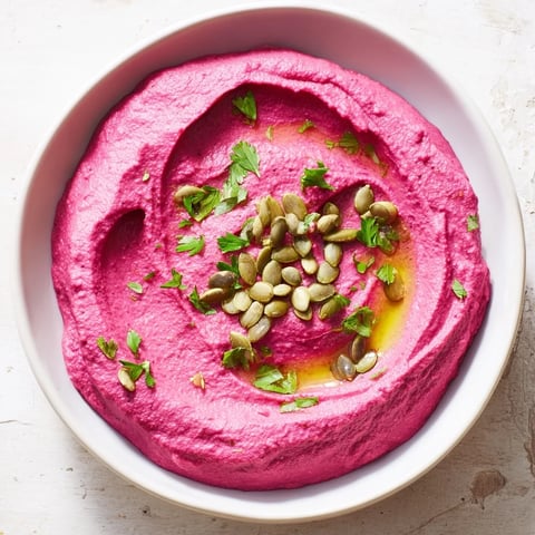 Vibrant beet hummus swirled beautifully with olive oil and sprinkled with toasted seeds for serving.