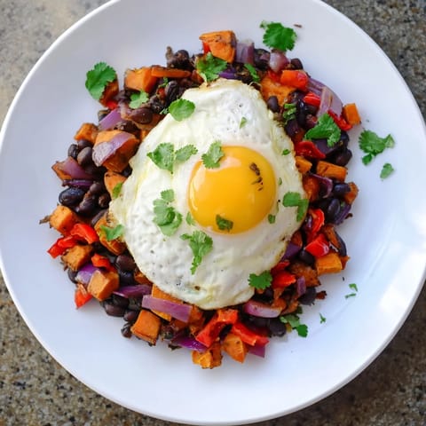 A skillet brimming with delicious sweet potato & black bean breakfast hash topped with eggs.