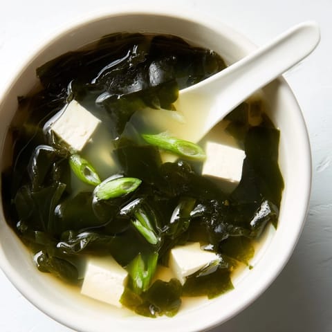 In a ceramic bowl, wakame soup glistens with aromatic dashi broth, silken tofu, and fresh sliced scallions.