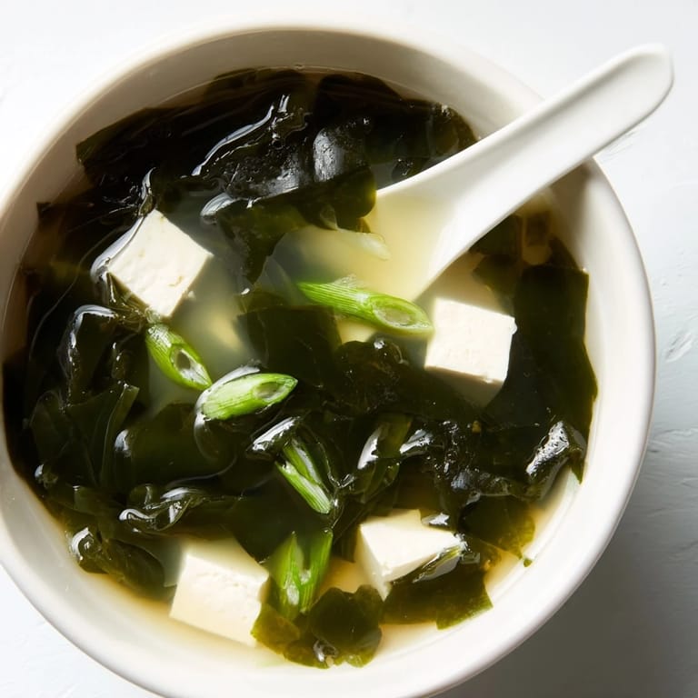 In a ceramic bowl, wakame soup glistens with aromatic dashi broth, silken tofu, and fresh sliced scallions.