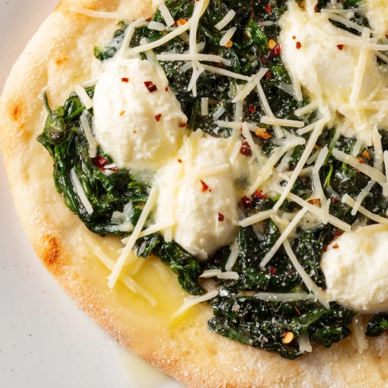 Crispy thin-crust spinach ricotta pizza topped with creamy dollops, garlic butter, and Parmesan served beside a glass of white wine.