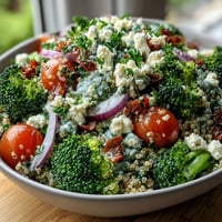 A colorful grain bowl with quinoa, broccoli, peas, and feta, drizzled with lemon-Dijon dressing for a fresh, satisfying meal.  